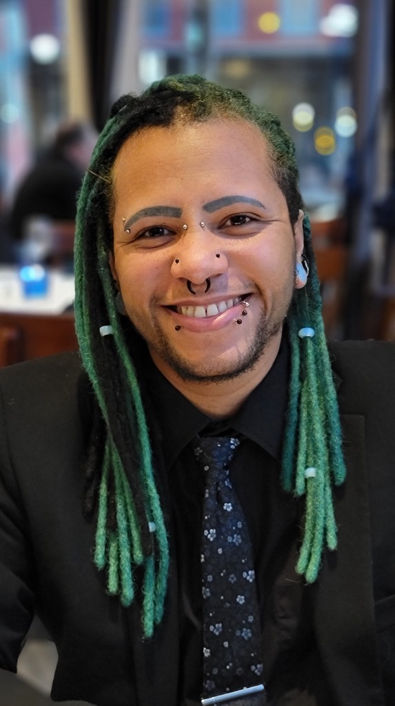 A picture of Dr. Graves, a Black man with piercings and green locks, smiling.