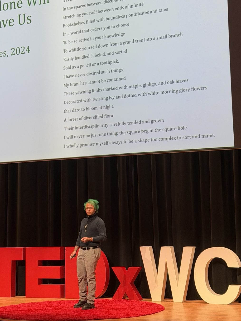 Projected slide displaying Kei Graves' 2024 poem titled 'Beauty Alone Will Not Save Us,' with lines of verse visible about interdisciplinary knowledge and botanical imagery, speaker standing below on stage with dark curtains.